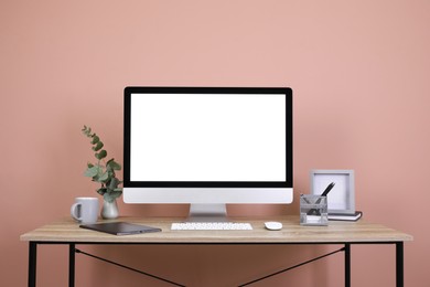 Photo of Modern computer with blank screen on desk near pink wall, space for design. Comfortable workplace