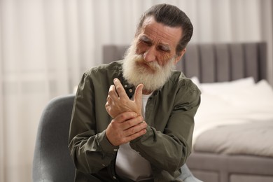 Photo of Senior man suffering from pain in hand at home. Rheumatism symptom