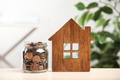 Photo of House model and glass jar with coins on table. Money savings