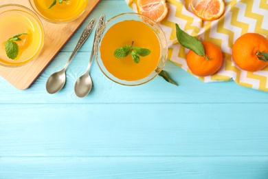 Photo of Delicious tangerine jelly and fresh fruits on light blue wooden table, flat lay. Space for text