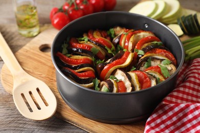 Photo of Delicious ratatouille in round baking pan and spatula on table