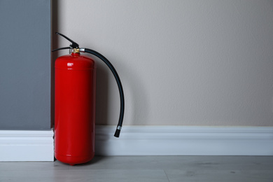 Photo of Fire extinguisher near light wall indoors. Space for text