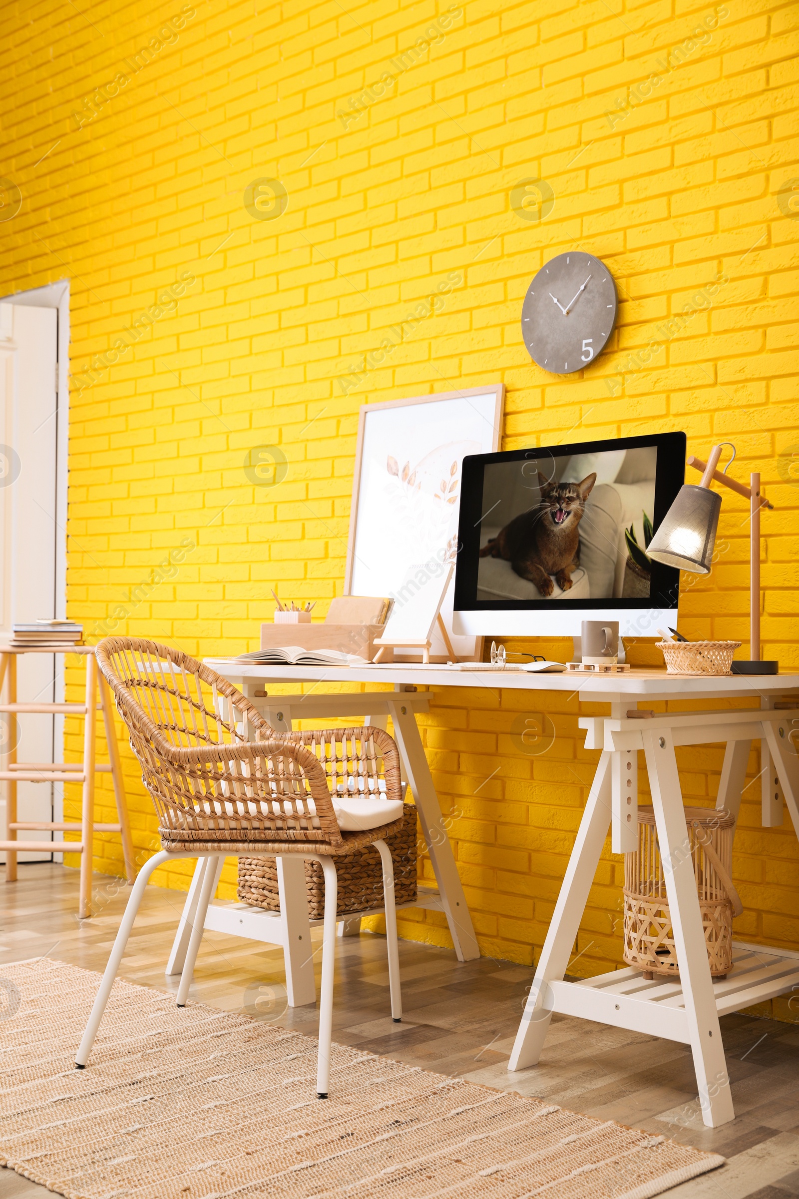 Stylish home office interior with comfortable workplace near yellow brick wall Photo of Stylish home office interior with comfortable workplace near yellow brick wall