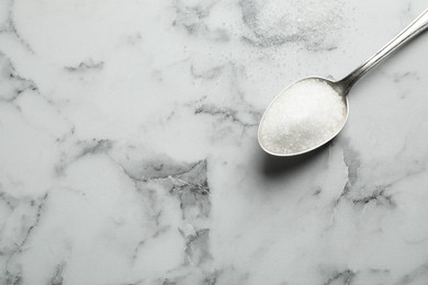 Photo of Spoon of white sugar on marble table, top view. Space for text