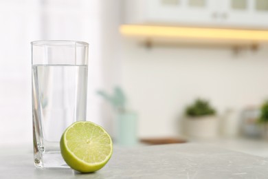 Filtered water in glass and lime on light table in kitchen, closeup. Space for text