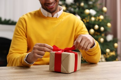 Photo of Man opening Christmas gift box at wooden table in room, closeup