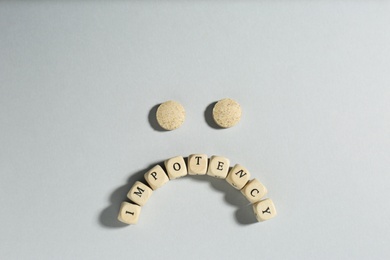 Photo of Sad face made of pills and cubes with word Impotency on light grey background, flat lay