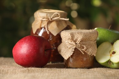 Photo of Delicious apple jam and fresh fruits on burlap against blurred background, closeup