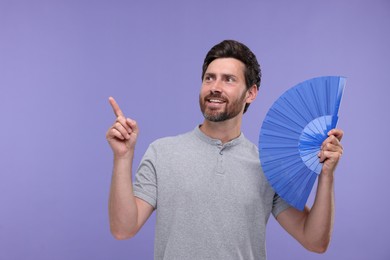 Photo of Happy man holding hand fan on purple background. Space for text