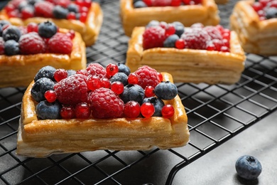 Photo of Cooling rack and fresh delicious puff pastry with sweet berries on grey table, closeup