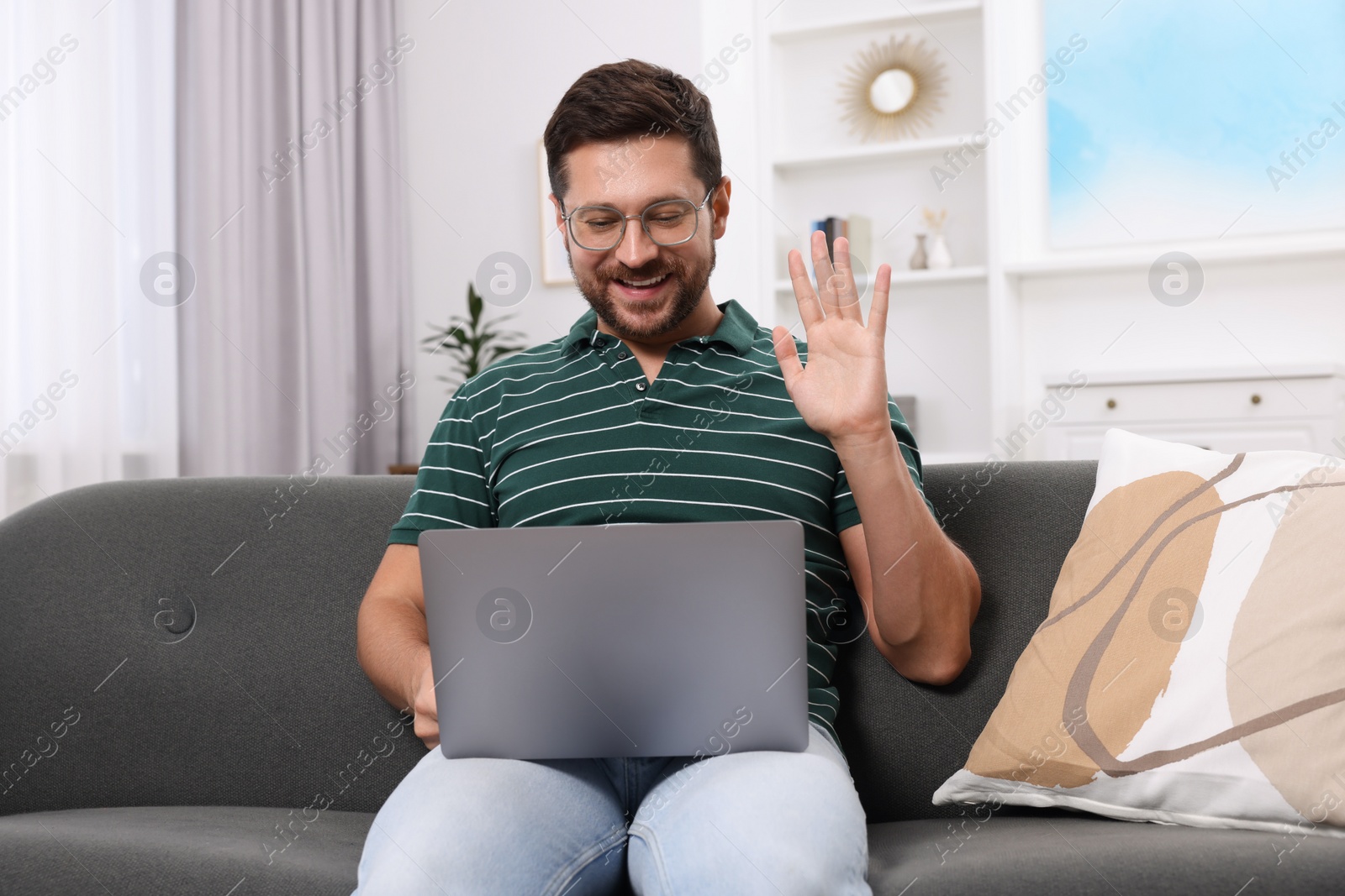 Photo of Happy man greeting someone during video chat via laptop at home