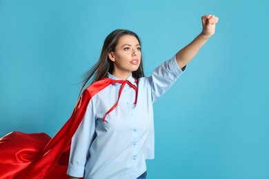 Photo of Confident young woman wearing superhero cape on light blue background