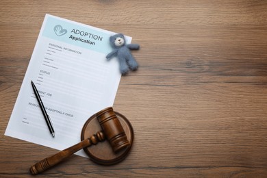 Photo of Adoption application, gavel, toy bear and pen on wooden table, flat lay. Space for text