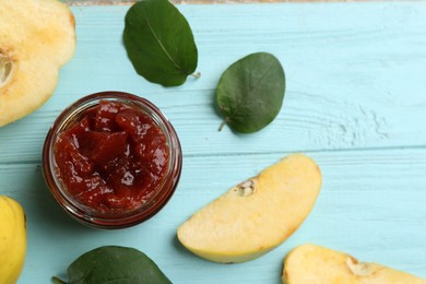 Delicious quince jam, fruits and leaves on light blue wooden table, flat lay