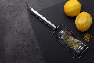 Photo of Grater and fresh lemons on black table, flat lay. Space for text
