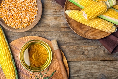 Flat lay composition with bowl of corn oil, cobs and kernels on wooden background