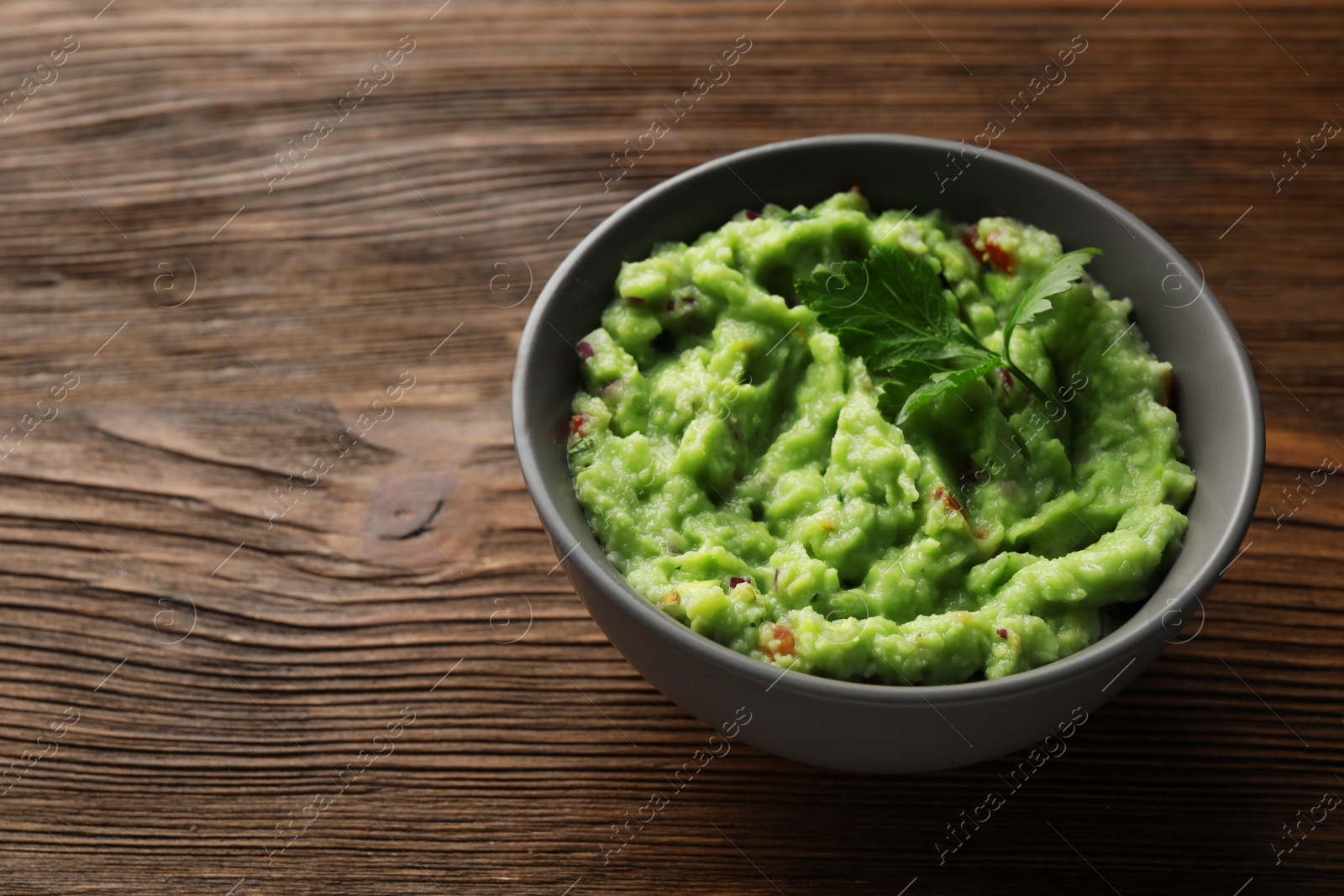 Bowl of delicious guacamole with parsley on wooden table, space for text Photo of Bowl of delicious guacamole with parsley on wooden table, space for text