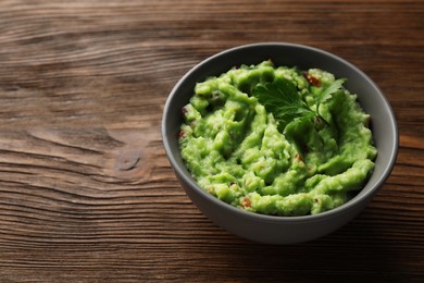 Photo of Bowl of delicious guacamole with parsley on wooden table, space for text