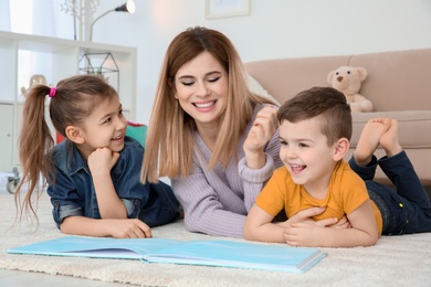 Photo of Little children with their nanny lying on floor and reading book at home