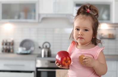 Photo of Adorable baby girl with apple and tasty cookie in kitchen. Space for text