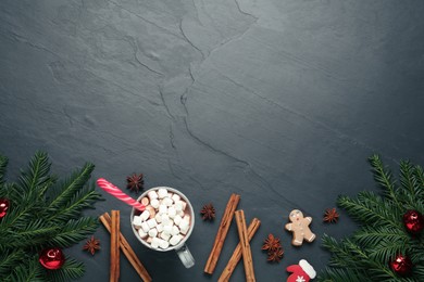 Photo of Delicious hot chocolate with marshmallows and candy cane near Christmas decor on black table, flat lay. Space for text