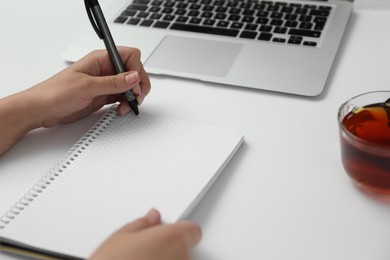 Photo of Left-handed woman writing in notebook at table, closeup