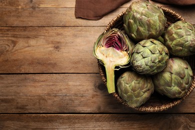 Photo of Cut and whole fresh raw artichokes in basket on wooden table, top view. Space for text
