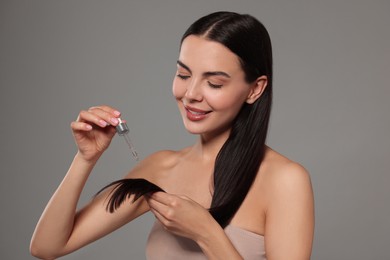 Photo of Beautiful woman applying hair serum on grey background. Cosmetic product