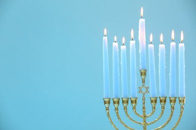 Photo of Hanukkah celebration. Menorah with burning candles on light blue background, space for text