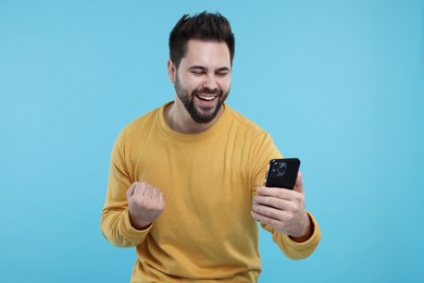 Photo of Happy young man using smartphone on light blue background