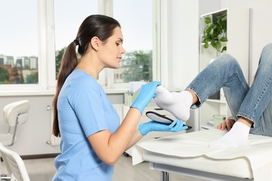 Beautiful female orthopedist fitting insole to patient's foot in hospital