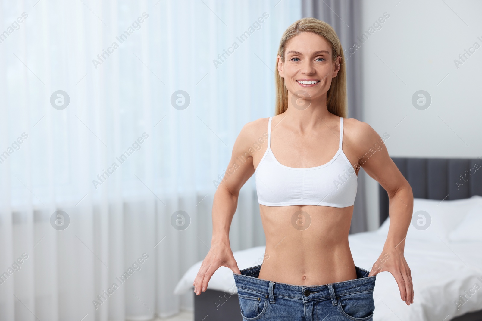 Photo of Slim woman wearing big jeans at home, space for text. Weight loss