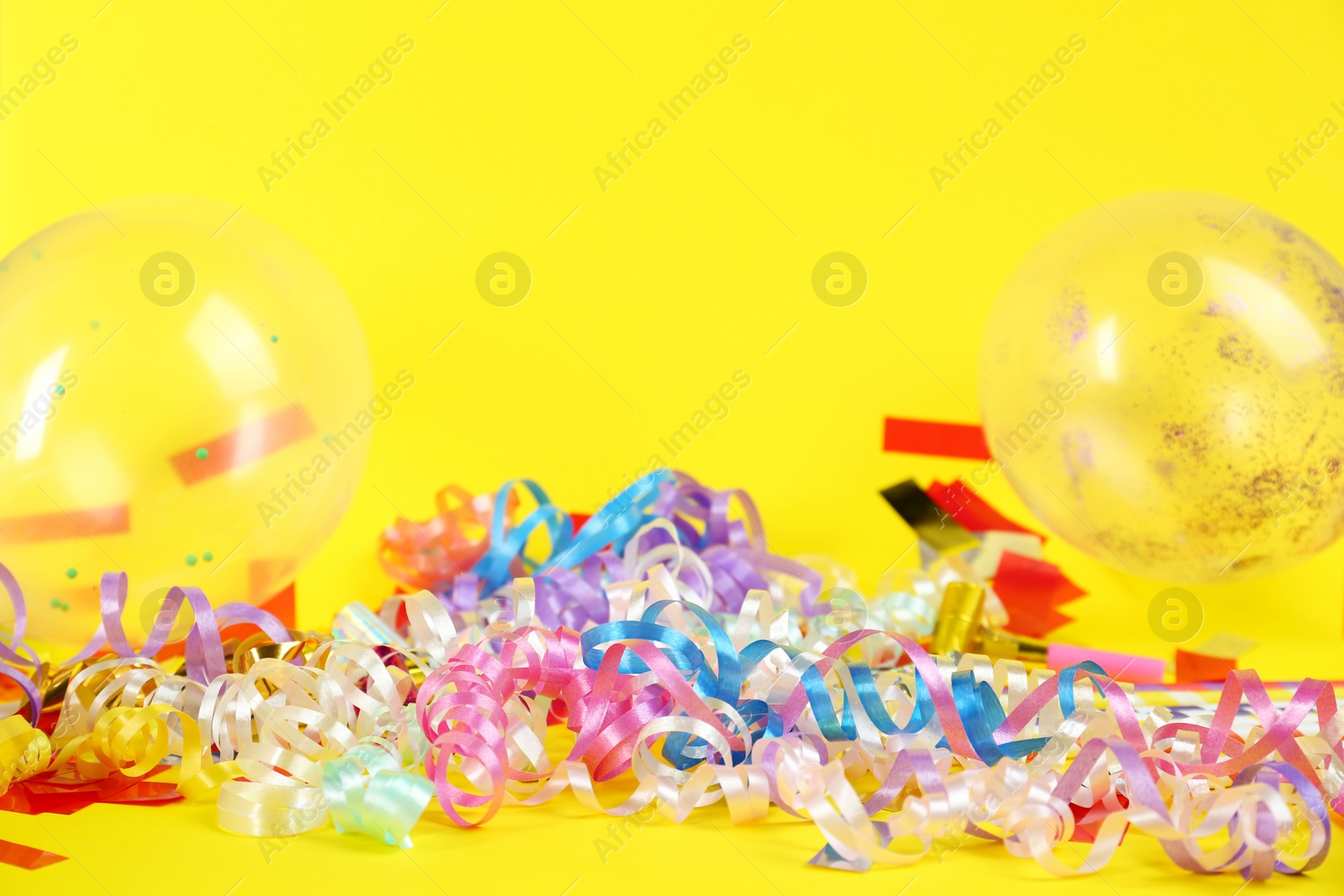 Photo of Colorful serpentine streamers, confetti and balloons on yellow background, space for text