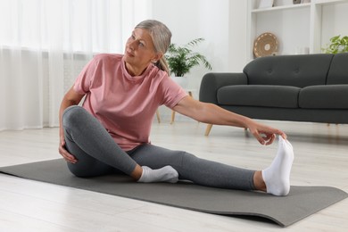 Senior woman in sportswear stretching on fitness mat at home