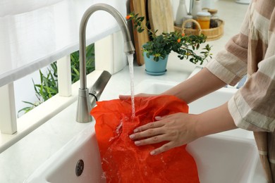 Photo of Woman washing beeswax food wrap under tap water in kitchen sink, closeup