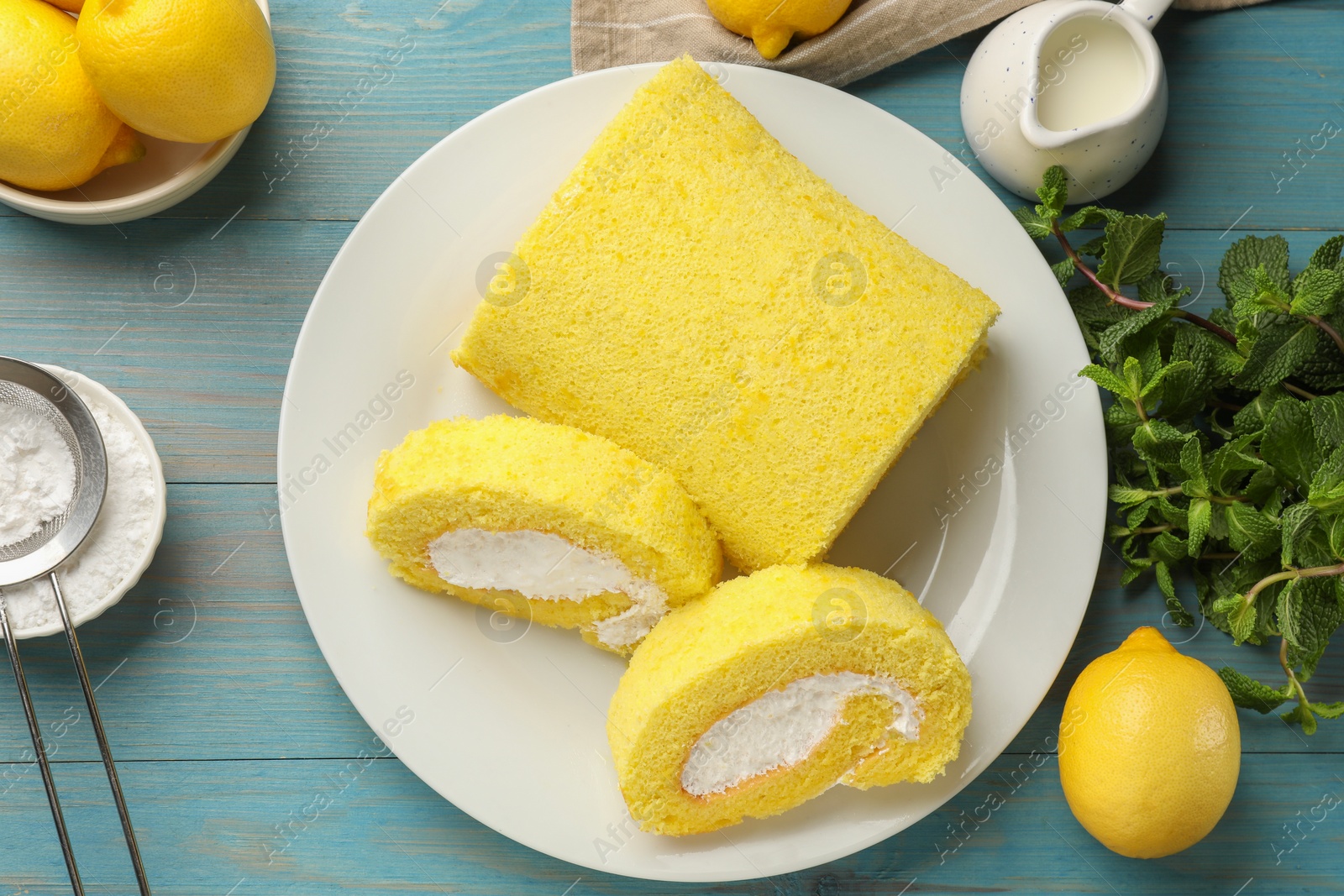 Delicious cake roll, lemons, mint and powdered sugar on light blue wooden table, flat lay Photo of Delicious cake roll, lemons, mint and powdered sugar on light blue wooden table, flat lay