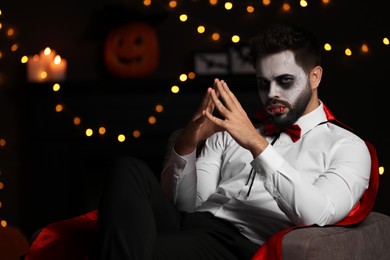 Photo of Man in scary vampire costume against blurred lights indoors, space for text. Halloween celebration