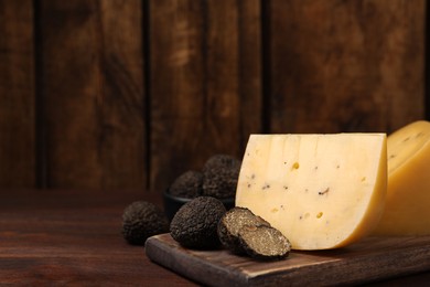 Photo of Delicious cheese and fresh black truffles on wooden table. Space for text
