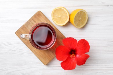 Photo of Delicious hibiscus tea, halves of lemon and beautiful flower on white wooden table, flat lay