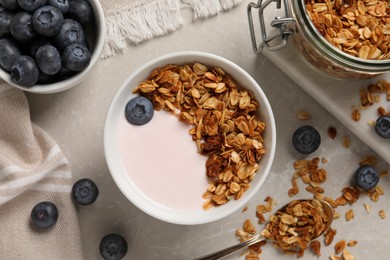 Photo of Delicious yogurt with granola and blueberries served on grey marble table, flat lay