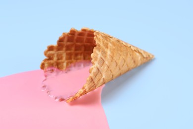 Photo of Melted ice cream and wafer cone on light blue background, closeup