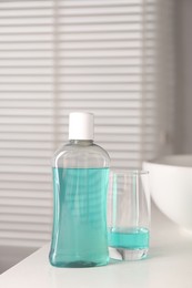 Bottle and glass of mouthwash on white countertop in bathroom