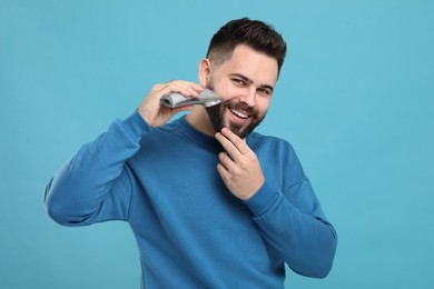 Photo of Handsome young man trimming beard on light blue background