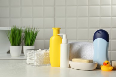 Photo of Baby cosmetic products, bath duck, cotton swabs and towel on white table against tiled wall