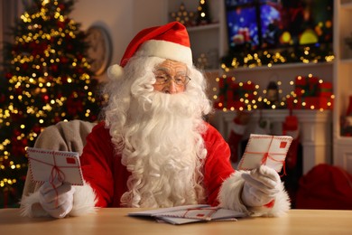 Photo of Santa Claus holding letters at table in room decorated for Christmas