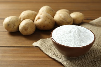 Photo of Bowl with starch and fresh potatoes on wooden table, space for text
