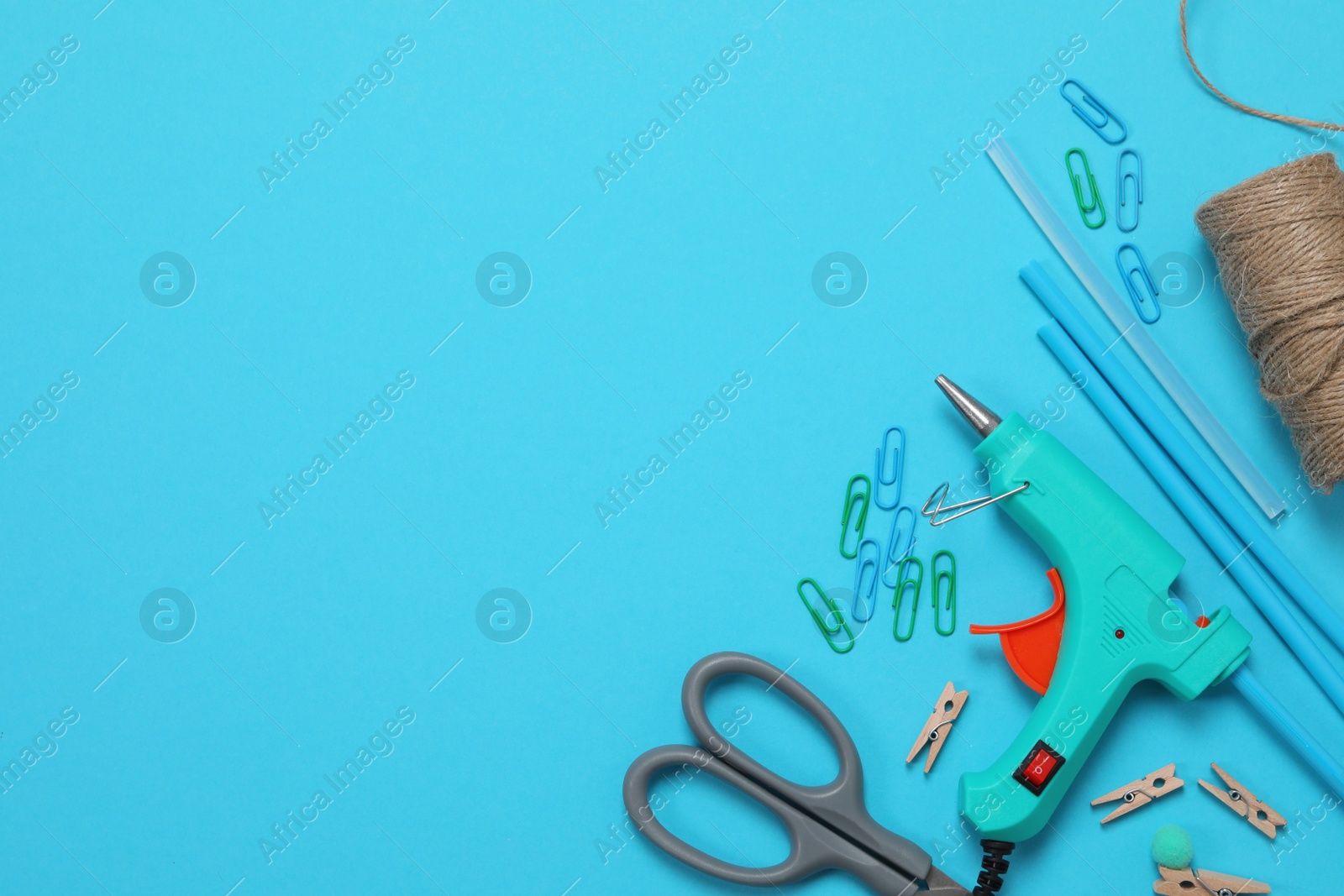 Photo of Hot glue gun and handicraft materials on light blue background, flat lay. Space for text