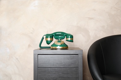 Photo of Green vintage corded phone on chest of drawers near beige wall