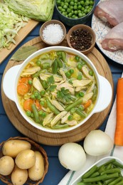 Photo of Saucepan of delicious vegetable soup with chicken and different ingredients on blue wooden table, flat lay