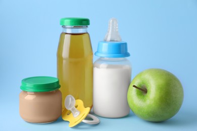 Healthy baby food, juice, milk, apple and pacifier on light blue background